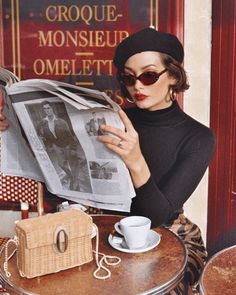 a woman sitting at a table with a newspaper in front of her and a cup of coffee