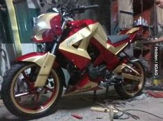 a red and gold motorcycle parked inside of a garage next to a man working on it