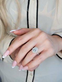 a woman's hand with a diamond ring on her left hand and pink manicured nails