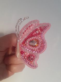 a hand holding a pink butterfly brooch with pearls on it's back and wings