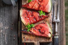 slices of watermelon on a wooden cutting board with knife and fork next to it