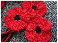 crocheted red flowers with black centers sitting on a gray surface next to yarn balls