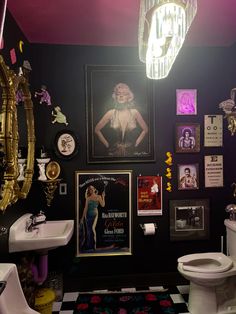 a bathroom decorated in black and white with pictures on the wall, sink, toilet and chandelier