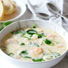 a bowl of soup with shrimp and spinach in it next to bread on the side