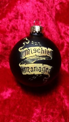 a black ornament with gold writing on it sitting on a red velvet surface