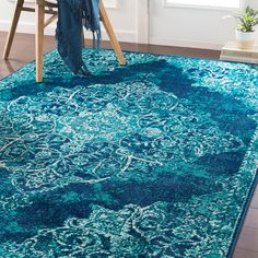 a blue area rug with an ornate design on the top and bottom, in front of a chair