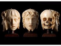 three carved ivory heads on wooden bases, one with a skull and the other with an angel's head