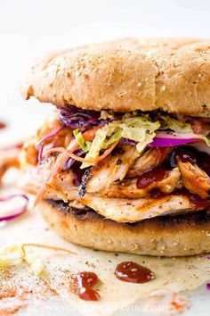 a chicken sandwich with coleslaw, lettuce and red onions on a bun