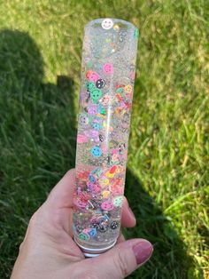 a person holding up a plastic tube filled with confetti and buttons in the grass