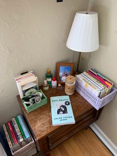 a table with books, magazines and a lamp on it next to a wall in a room