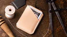 a leather wallet sitting on top of a wooden table next to scissors and spools of thread