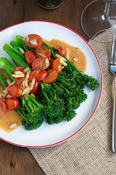 a white plate topped with broccoli, tomatoes and other vegetables next to a fork