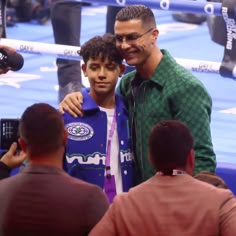 two men standing next to each other in front of a boxing ring with one man holding his arm around the other