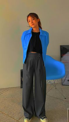 a woman standing in front of a chair wearing black pants and a blue blazer