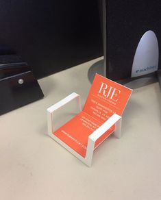 an orange and white business card holder sitting on top of a desk next to a computer