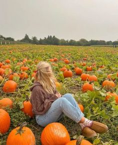 a woman sitting in the middle of a field of pumpkins on a cloudy day