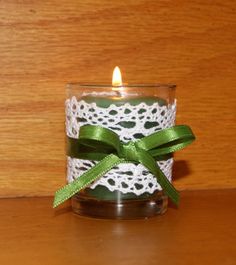 a candle with a green ribbon around it sitting on a table next to a wooden wall