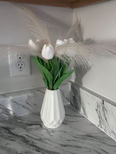 a white vase filled with flowers on top of a marble countertop next to a light switch