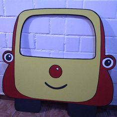 a yellow and red toy car sitting in front of a brick wall with eyes on it