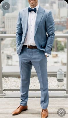 a man in a blue suit and bow tie standing on a wooden deck with his hands in his pockets