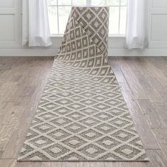 a white and beige area rug on the floor in front of a window with curtains