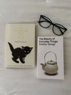 a book and glasses sitting on top of a bed next to an open teapot