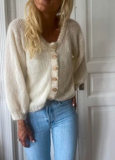 a woman standing in front of a white door wearing jeans and a cardigan sweater