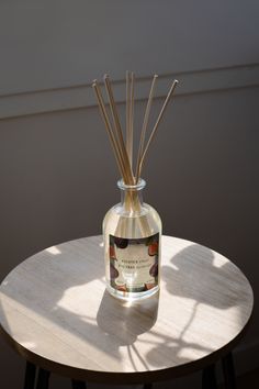 a glass bottle filled with reeds sitting on top of a table next to a round wooden table