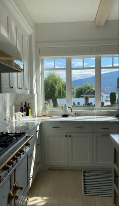 a large kitchen with white cabinets and stainless steel stove top oven next to a window