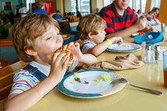 two young boys sitting at a table with plates of food in front of them, while an adult looks on