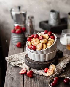 a bowl filled with cherries sitting on top of a wooden table next to other dishes