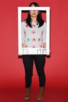 a woman standing in front of a red background holding up a white frame with flowers on it