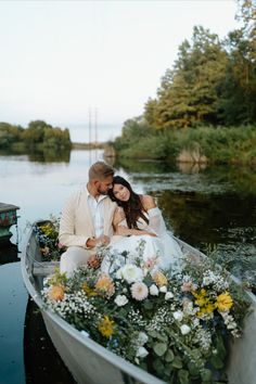 a bride and groom are sitting in a boat with flowers on the front, surrounded by greenery