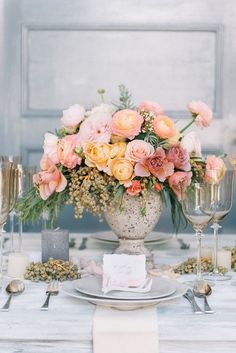 a table topped with a vase filled with pink and yellow flowers next to wine glasses