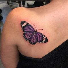 a purple butterfly tattoo on the back of a woman's upper arm and shoulder