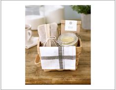 a basket filled with tea towels and soap on top of a wooden table next to a cup