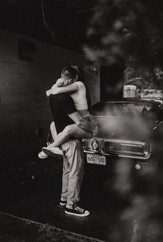 black and white photograph of two people hugging in front of a car