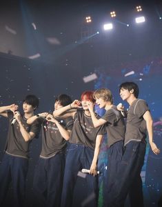 group of young men standing on stage with their arms around each other and confetti falling in the air