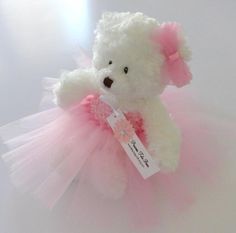 a white teddy bear wearing a pink tutu with a tag on it's chest