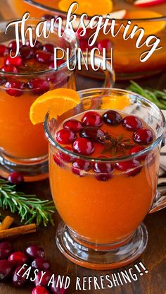 two glasses filled with oranges and cranberries on top of a wooden table