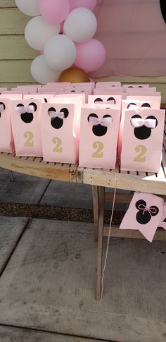 pink bags with numbers are sitting on a wooden table in front of balloons and streamers