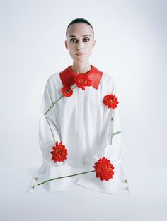 a woman wearing a red hat with flowers on her head and white dress, sitting in front of a white background