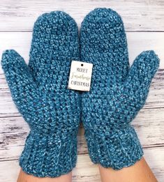 a pair of blue knitted mittens with a tag on the front saying merry christmas