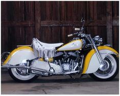 a yellow and white motorcycle parked in front of a wooden wall