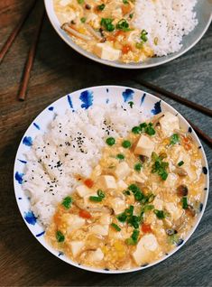 two plates filled with rice and tofu on top of a table next to chopsticks