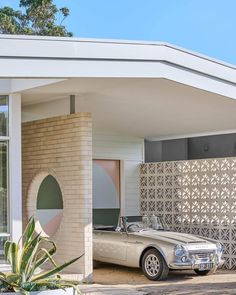 an old car is parked in front of a house with a decorative wall behind it