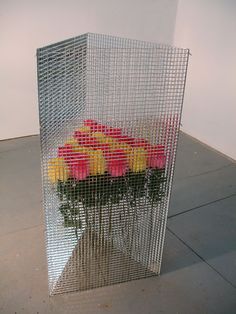 a vase filled with flowers sitting on top of a cement floor next to a white wall