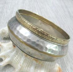 A pair of matching Vintage brass bracelets in boho style, can be worn as a set or each one separately. These bracelets were a travel souvenir from India, made in the 1980s.Wide bracelet: silver plated brass, 14 mm wide and 6-7 mm thick with textured hammered surface and a rib around the middle. The silver plate is a bit worn off, the edges and the rib looks gold color. Narrow bracelet: 6 mm wide, gold plated brass with textured surface, the pattern looks like flowers and leaves.Length: 8 inches Silver Brass Spiritual Bracelets, Spiritual Silver Brass Bracelets, Silver Spiritual Brass Bangle, Spiritual Silver-colored Brass Bangle, Festival Brass Bracelets In Silver Color, Silver Brass Bracelets For Festival, Bohemian Metal Bangle Nickel-free, Silver Brass Bangle For Festival, Silver Bohemian Brass Bangle