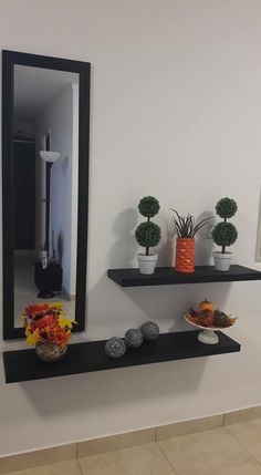 two black floating shelves with plants and bowls on them in front of a mirror that is reflecting the bathroom