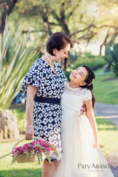 two women standing next to each other in front of trees and grass with pink flowers